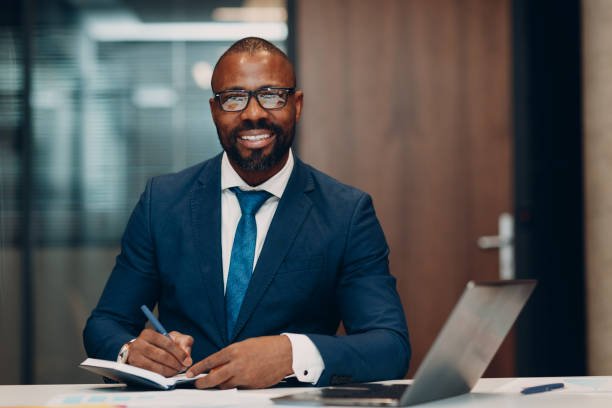 Portrait smiling african american businessman in blue suit sit at table for meeting in office with notebook with pen and laptop